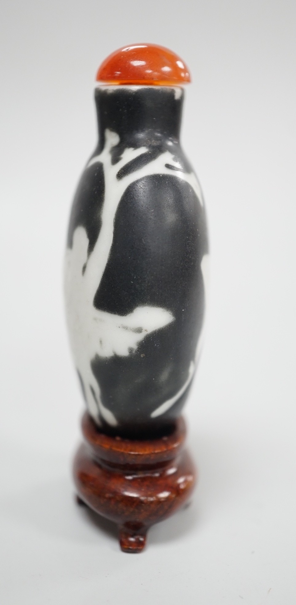 A Chinese porcelain white on black ground silhouette snuff bottle, 5.6 cm excluding stopper and wood stand